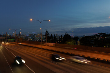 Vehicles driving through I-5 with Seattle skyline as the backdrop against a night sky. 
