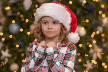 Kid praying, kids prayer. Happy funny child in Santa hat near Christmas tree. Christmas and New Year concept.