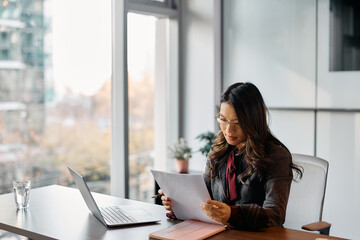 Young Asian businesswoman analyzing reports while working in office.