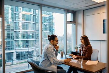 Happy businesswoman using laptop while analyzing reports with male coworker in office.