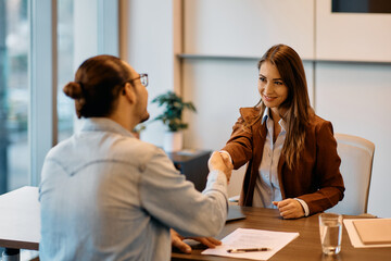 Happy human resource manager handshaking with male candidate on job interview in office.