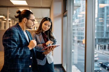 Multiracial business colleagues analyzing reports on touchpad while working in office.