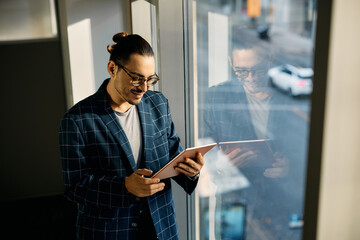 Happy Hispanic businesswoman working on digital tablet by window in office.