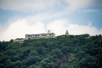 Concrete building with temple spire on top peak of aravalli range in jaipur against white monsoon...
