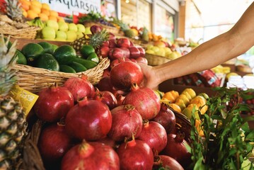 Woman choosing pomegranate among many others while having great food shopping at the local food market. Stock photo. High quality photo