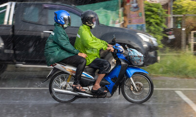 Couple in raincoats drive in rain, Thailand
