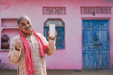 Indian old man showing smartphone screen at his home