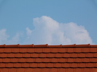 sloped red clay roof ridge detail. new bright clay house roof tiles. construction industry and building materials concept. clear blue sky. bright sunlight