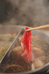 Using chopsticks to bring the fresh beef to the Sukiyaki pot. Japanese shabu-shabu or Sukiyaki.