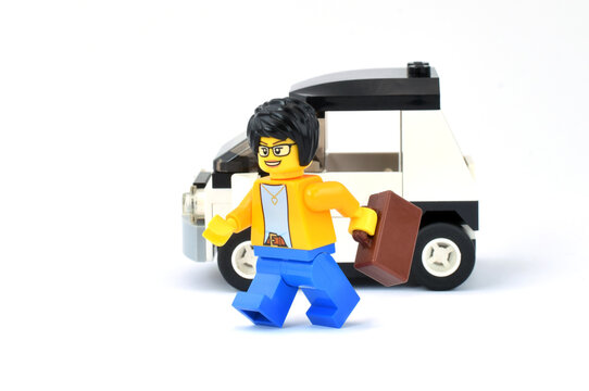 Lego minifigure of business lady is standing in front of car. Editorial illustrative image of auto lady in the city. Studio shot.