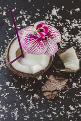 Top down view of fresh coconut with straw which decorated with orchid on stone black table. Tropic