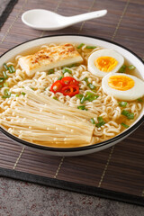 Ramen soup with tofu cheese, enoki mushrooms, noodles, green onions and chili peppers close-up in a bowl on the table. Vertical