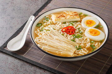 Spicy miso ramen soup with tofu, enoki mushrooms, noodles, green onion and chili close-up in a bowl on the table. Horizontal