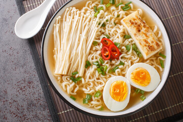 Homemade Ramen soup with marinated tofu, enoki mushrooms, noodles, green onions and chili peppers close-up in a bowl on the table. Horizontal top view from above