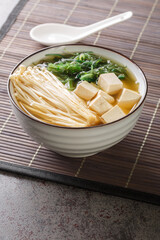 Japanese vegetarian shiro miso soup with tofu, enoki mushrooms, wakame seaweed close-up in a bowl on the table. Vertical