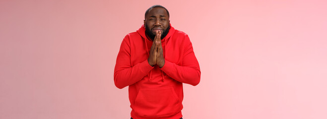 Miserable african american man beard in red hoodie stooping make supplicating upset grimace grying sobbing asking help say please hold hands pray begging mercy, apologizing need money