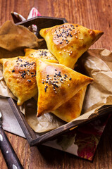 Traditional Arabic baked samosa with minced meat and vegetable served as close-up on a wooden tray