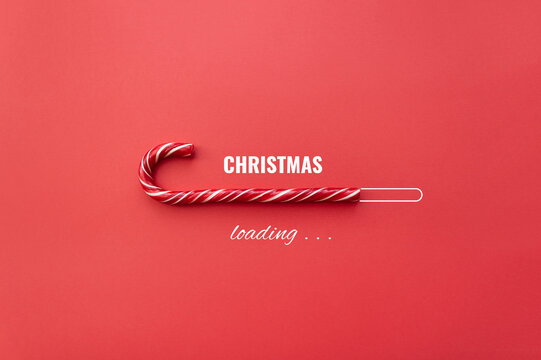 Striped candy cane and lettering Christmas loading on red background. Concept of waiting for seasonal holidays. Copy space, selective focus