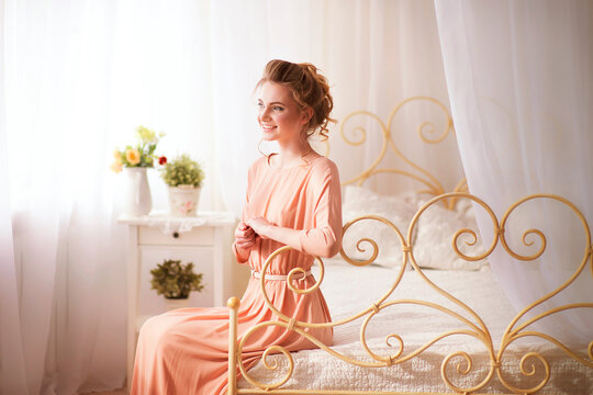 The concept of women's day, tenderness . A girl in a pink dress is sitting on a bed in a room with a vintage interior. Large size, calm tones in the photo. suitable for advertising insurance companies