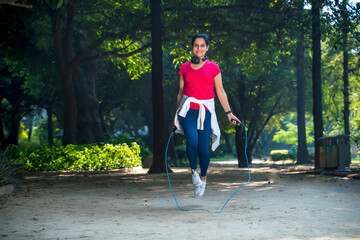 young Indian woman with jump rope and doing skipping workout in a park.