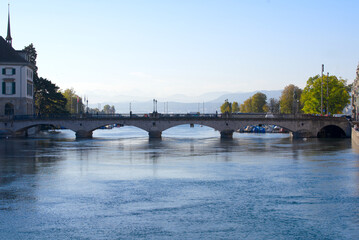 Fototapeta premium Beautiful cityscape of the old town of Zürich with Limmat River in the foreground and Minster Bridge in the back on a sunny late summer morning. Photo taken September 22nd, 2022, Zurich, Switzerland.
