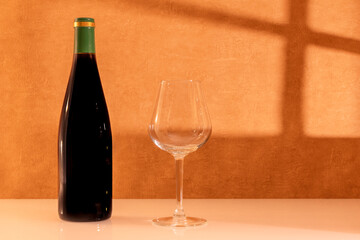 Verre de vin rouge avec une bouteille de vin sans étiquette avec rayons du soleil à travers une fenêtre.