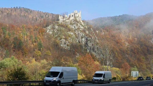 STRECNO, SLOVAKIA - OCTOBER 31, 2022: Cars passing on the road under the ruins of the Starhrad medieval castle in autumn.