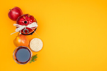 Gift pomegranate with a horseshoe for good luck, apples, traditional bread and a glass of red wine on a yellow background