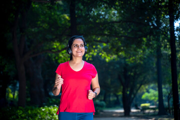 young indian woman with earphones listening music during jogging at park.