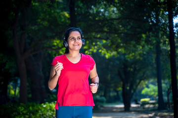 young indian woman with earphones listening music during jogging at park.