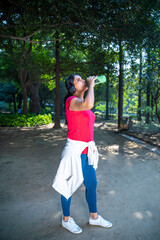 Indian woman drinks water from a bottle after running in the park.