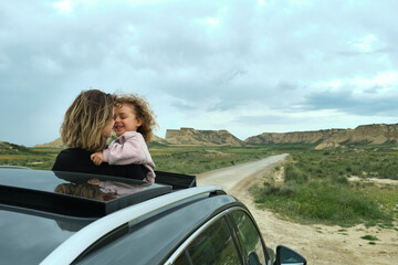 mother and daughter cuddling on the uncovered roof of a car, happily enjoying the sights of a road...