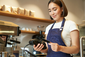 Cute asian girl, barista in cafe processing contactless payment, insert credit card into POS...