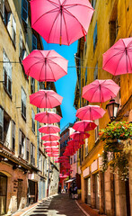 Fototapeta na wymiar Historic tenement houses and narrow streets decorated with pink umbrellas of old town quarter of perfumery city of Grasse in south France