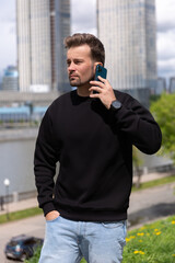 City portrait of handsome hipster guy with beard wearing black blank hoodie or sweatshirt with...