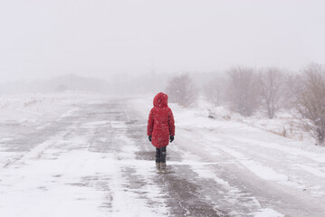 A lonely girl in a red jacket in a winter field in a blizzard.Rear view. The concept of loneliness. - 552772520