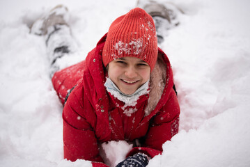 Fototapeta na wymiar A girl in a red jacket in the snow. The girl smiles and lies on the snow. Winter fun.