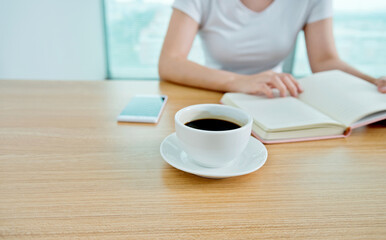 Woman reading book with cup of coffee on table