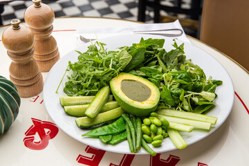 Green plate with lettuce, arugula, avocado, cucumbers and green peas