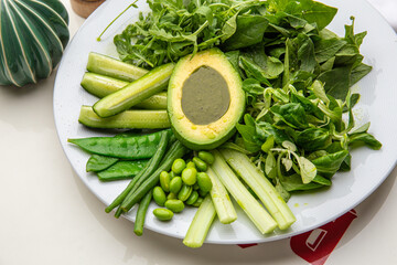 Green plate with lettuce, arugula, avocado, cucumbers and green peas