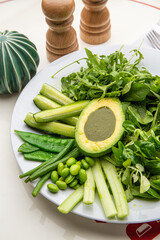 Green plate with lettuce, arugula, avocado, cucumbers and green peas