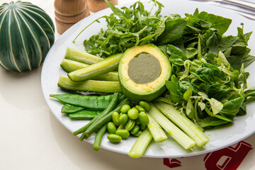 Green plate with lettuce, arugula, avocado, cucumbers and green peas