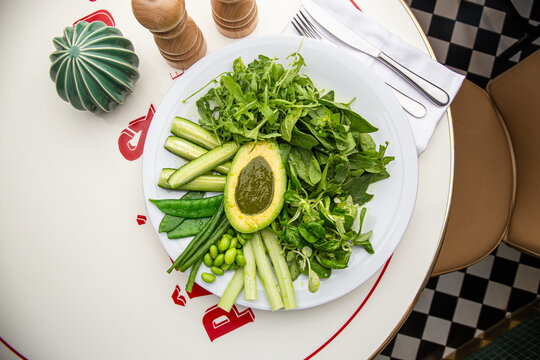 Green plate with lettuce, arugula, avocado, cucumbers and green peas