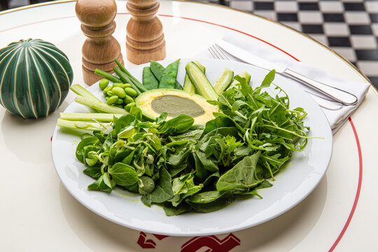 Green plate with lettuce, arugula, avocado, cucumbers and green peas