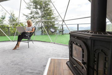 middle aged woman uses a laptop resting and spending time at Glamping house on holidays. holiday dome tent. Cozy, camping, hygge, lifestyle concept
