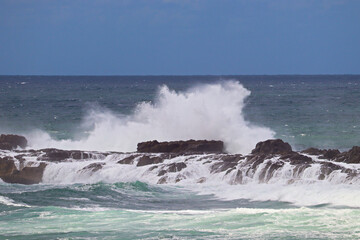 Waves crashing over the rocks near Fingal Bay, with a container or cargo ship in the background.