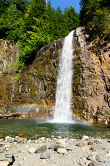 Fototapeta na wymiar Waterfall surrounded by trees and rocks with a rainbow at the bottom
