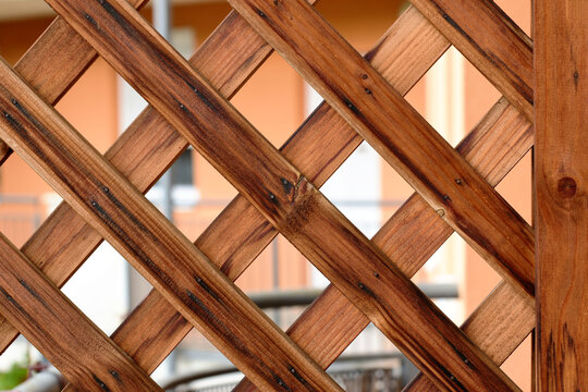Brown wood trellis macro. pine wood privacy screen or lattice detail. narrow strips fastened with small metal nails. diamond shape pattern. flat brown wood strips. soft blurred residential background