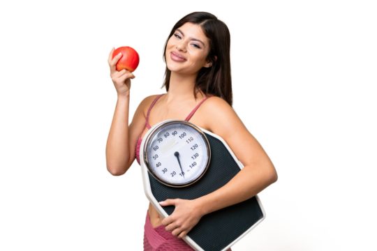 Young Russian woman with rainproof coat and umbrella over isolated chroma key background with weighing machine and with an apple