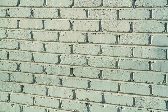 White gray brick wall with dark grout in late afternoon shade on the side of building in the downtown city or in urban area